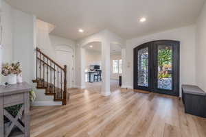Entryway with arched walkways, french doors, light wood-style flooring, stairs, and recessed lighting
