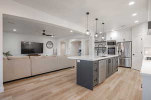Kitchen with appliances with stainless steel finishes, arched walkways, light countertops, open floor plan, and ceiling fan