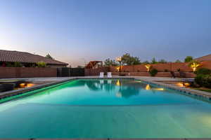 Pool at dusk with a fenced backyard and a patio area