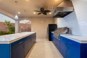 Kitchen featuring exhaust hood, blue cabinets, backsplash, light countertops, and recessed lighting