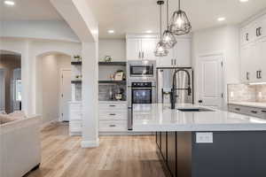 Kitchen with stainless steel appliances, arched walkways, open shelves, tasteful backsplash, and white cabinetry
