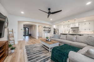 Living area with arched walkways, a ceiling fan, light wood-style floors, and recessed lighting