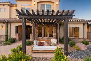 Back of property with a pergola, stone siding, stucco siding, a tile roof, and a patio