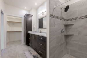 Full bathroom featuring tiled shower, vanity, a walk in closet, and recessed lighting