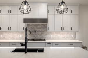 Kitchen with white cabinetry, decorative backsplash, light stone countertops, and pendant lighting