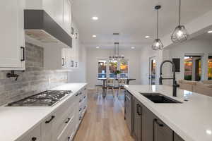 Kitchen featuring stainless steel gas stovetop, wall chimney range hood, light wood-type flooring, recessed lighting, and light stone counters