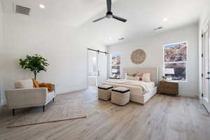 Bedroom with a barn door, light wood-style flooring, recessed lighting, a ceiling fan, and vaulted ceiling