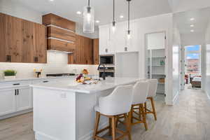 Kitchen with black microwave, decorative backsplash, light countertops, stainless steel oven, and an island with sink