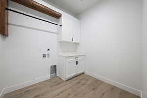 Washroom with hookup for an electric dryer, light wood finished floors, washer hookup, and cabinet space