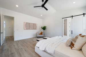 Bedroom featuring a barn door, lofted ceiling, recessed lighting, light wood finished floors, and a ceiling fan