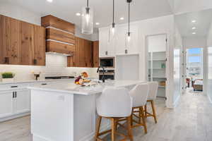 Kitchen with black microwave, light countertops, tasteful backsplash, stovetop, and a center island with sink