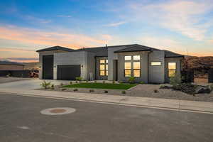 Contemporary house featuring a garage, driveway, a tiled roof, stucco siding, and a front yard