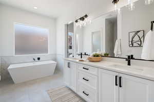 Full bath with tile walls, double vanity, a freestanding bath, tile patterned flooring, and a wainscoted wall