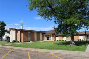 View of Church meetinghouse property featuring mature trees and uncovered paved parking