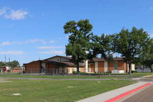 Side view of Church meetinghouse property with mature trees, chain link fence, and paved parking
