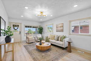 Living area with a textured ceiling, light wood-type flooring, a chandelier, and recessed lighting