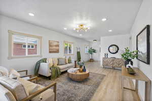 Living room featuring light wood-type flooring, a chandelier, recessed lighting, and a textured ceiling