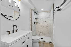 Bathroom featuring a marble finish shower, wood finished floors, and vanity