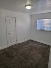 Empty room with dark colored carpet and a textured ceiling