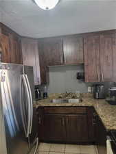 Kitchen with appliances with stainless steel finishes, a textured ceiling, light stone counters, light tile patterned floors, and dark brown cabinetry
