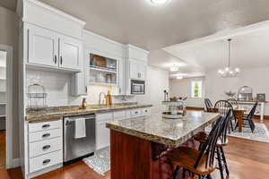 Kitchen featuring stainless steel dishwasher, a center island, dark wood-style floors, decorative backsplash