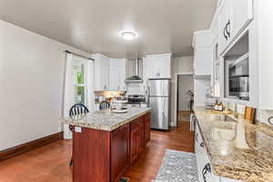 Kitchen with stainless steel appliances, wall chimney exhaust hood, dark wood-type flooring, white cabinets, and a textured ceiling