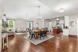 Dining room featuring a chandelier, plenty of natural light, dark wood-type flooring, Vaulted ceiling, and a textured ceiling