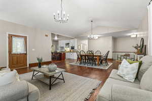 Living area with a chandelier, vaulted ceiling, and dark wood-style floors