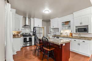 Kitchen with stainless steel appliances, wall chimney range hood, backsplash, a textured ceiling, and dark wood finished floors