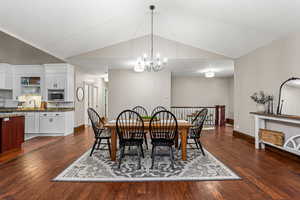 Dining area with Vaulted ceiling, a chandelier, and dark wood-style flooring