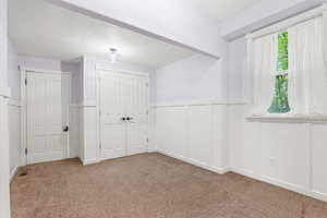 Unfurnished bedroom featuring wainscoting, carpet, a textured ceiling, a closet