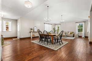 Dining space featuring a chandelier, plenty of natural light, dark wood-style floors, vaulted ceiling, and a textured ceiling