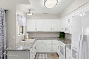 Kitchen with white appliances, white cabinets, and light wood-style flooring