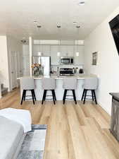 Kitchen with appliances with stainless steel finishes, a textured ceiling, a kitchen breakfast bar, light wood-style flooring, and light countertops