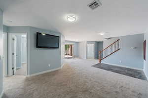 Unfurnished living room featuring carpet floors, stairway, and a textured ceiling