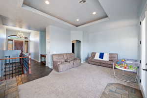 Carpeted living area with arched walkways, stone tile floors, a raised ceiling, recessed lighting, and a chandelier