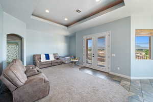 Living area with french doors, arched walkways, a raised ceiling, and recessed lighting