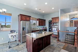 Kitchen with appliances with stainless steel finishes, a warming drawer, stone tile flooring, a chandelier, and a center island