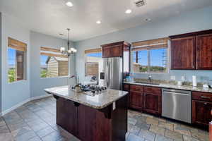 Kitchen with stainless steel appliances, a center island, a chandelier, light stone counters, and stone tile floors