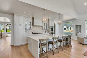 Kitchen with arched walkways, appliances with stainless steel finishes, premium range hood, an island with sink, and recessed lighting