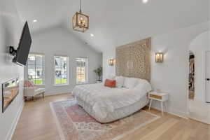 Bedroom featuring arched walkways, lofted ceiling, recessed lighting, wood finished floors, and a chandelier