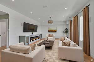 Living room with light wood finished floors, recessed lighting, and a glass covered fireplace