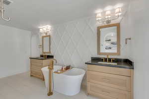 Full bath with two vanities, a freestanding bath, a decorative wall, and tile patterned floors