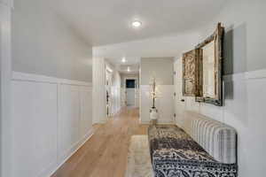 Hall with light wood-style floors, wainscoting, recessed lighting, and a decorative wall