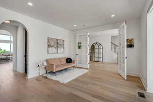 Sitting room featuring french doors, light wood-type flooring, recessed lighting, arched walkways, and stairway