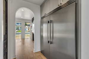 Hallway with arched walkways, light wood-type flooring, and recessed lighting