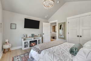 Bedroom with a chandelier, a closet, light wood finished floors, a glass covered fireplace, and high vaulted ceiling