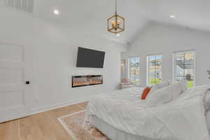 Bedroom featuring a glass covered fireplace, a chandelier, light wood finished floors, recessed lighting, and high vaulted ceiling