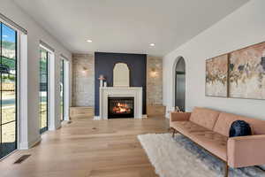 Living room featuring light wood finished floors, a glass covered fireplace, recessed lighting, and arched walkways