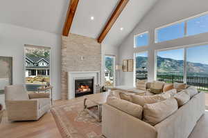 Living area featuring light wood-style flooring, high vaulted ceiling, beamed ceiling, plenty of natural light, and a fireplace